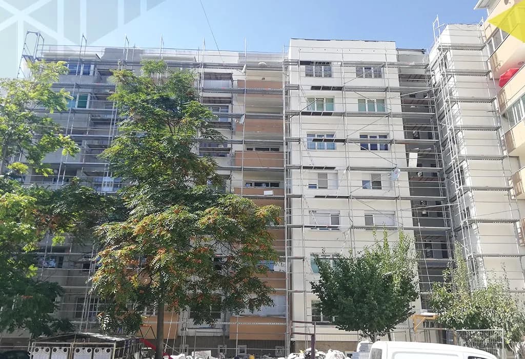 Фасадно скеле по цялата височина на панелен блок, с дървета пред него