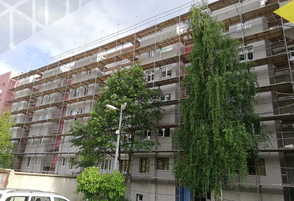 Фасадно скеле по жилищен блок, зад плачеща върба и улична лампа